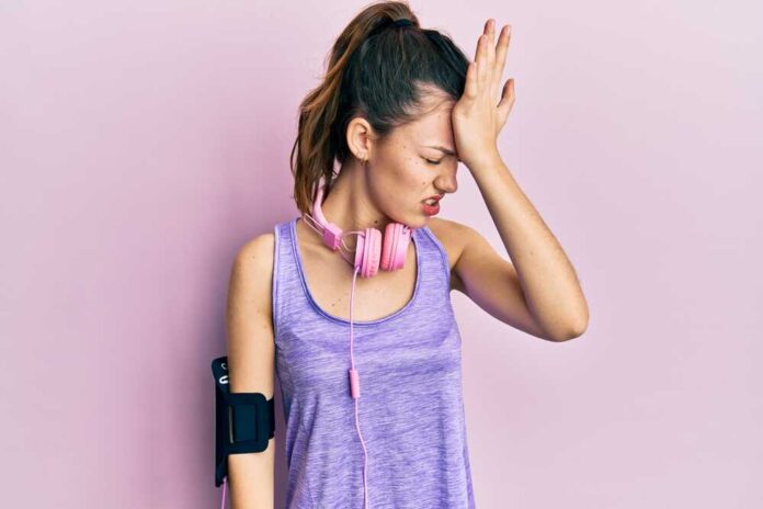 Young brunette woman wearing sportswear and headphones surprised with hand on head for mistake, remember error. forgot, bad memory concept.