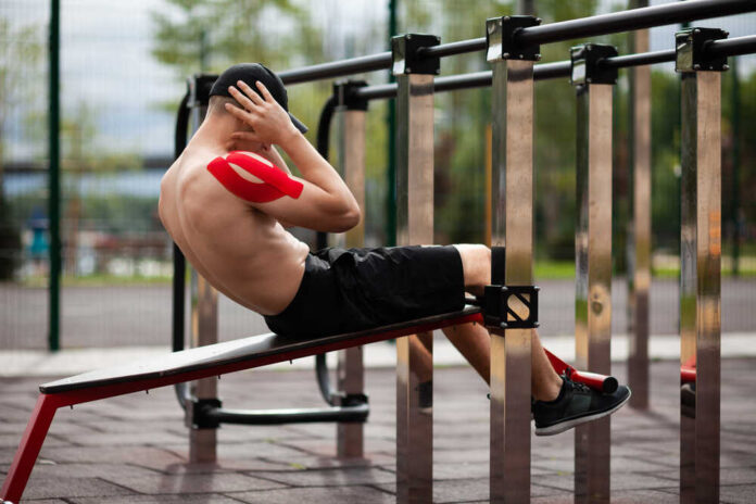 Young European athlete with injury is training outdoors. Kinesio